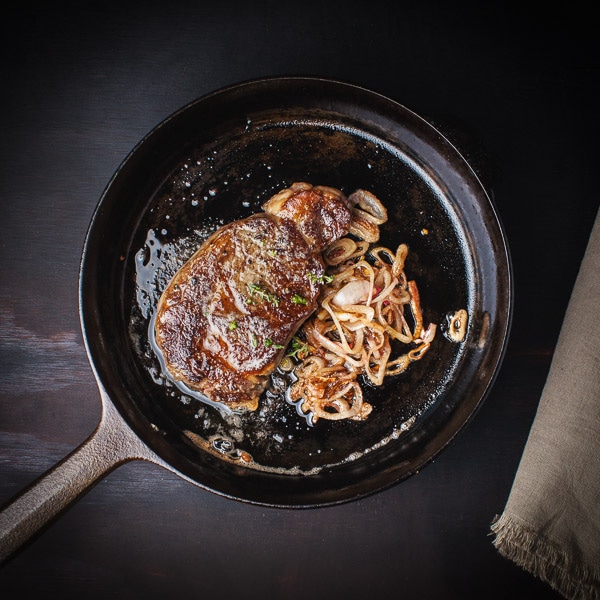 A steak with onions cooked in a cast iron skillet.