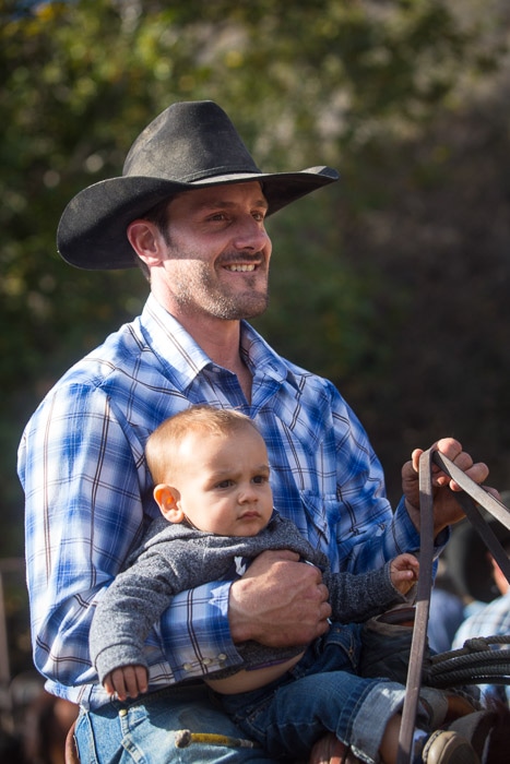 Hearst Ranch cowboy holding a toddler while horseback riding.