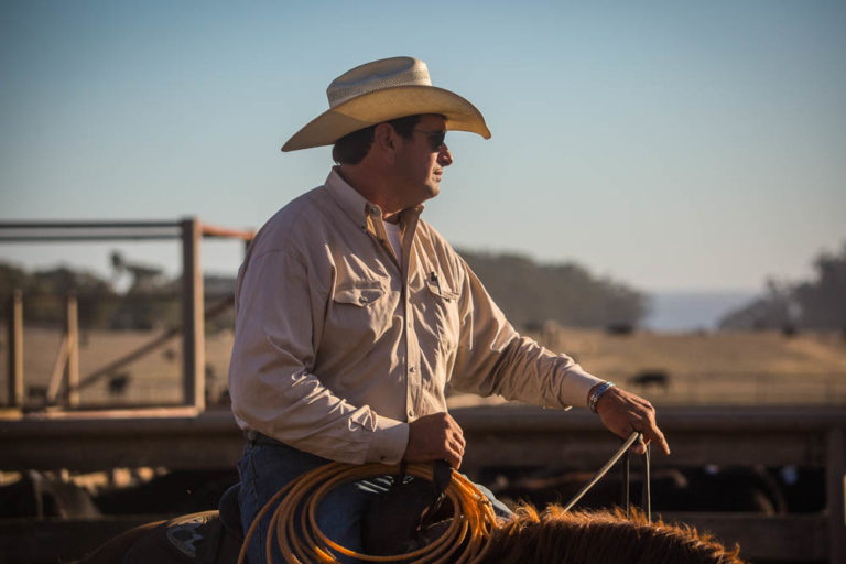 A Hearst Ranch Cowboy on a horse, wearing a cowboy hat and sunglasses.