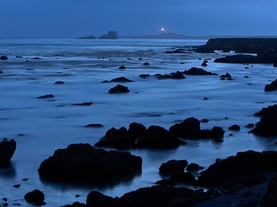 The San Simeon coast at night, with the Piedras Blancas Light Station illuminated in the background.