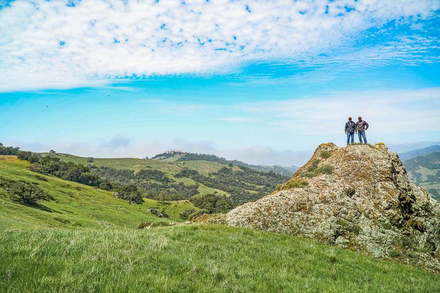 Two men standing on a rocky hill, with Hearst Castle in the background.