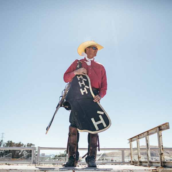 A cowboy holds equipment with the Hearst Ranch logo on it.