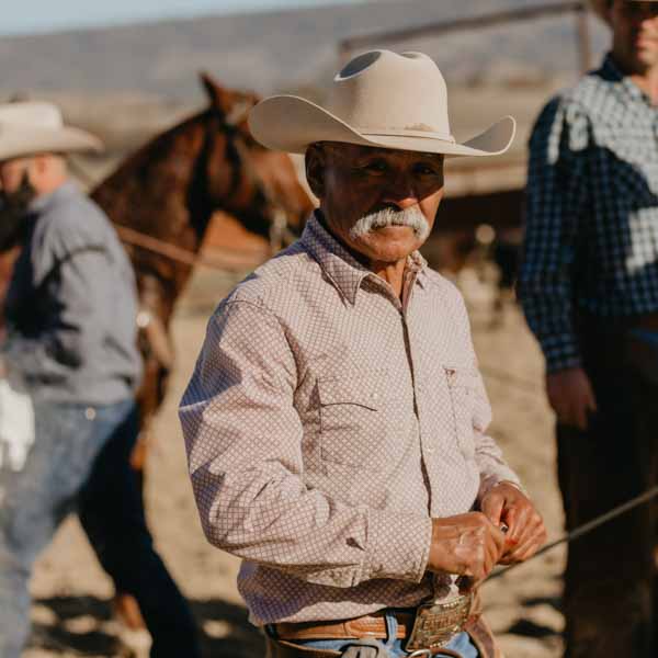 A Hearst Ranch cowboy wears a white cowboy hat, red striped shirt, and looks into the camera.