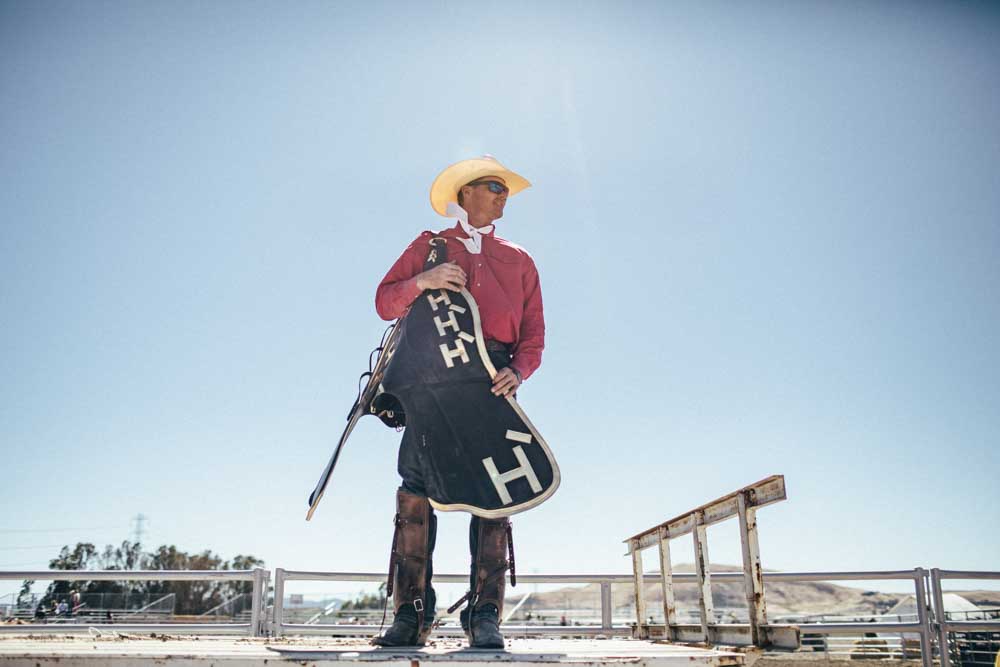 A cowboy holds equipment with the Hearst Ranch logo on it.