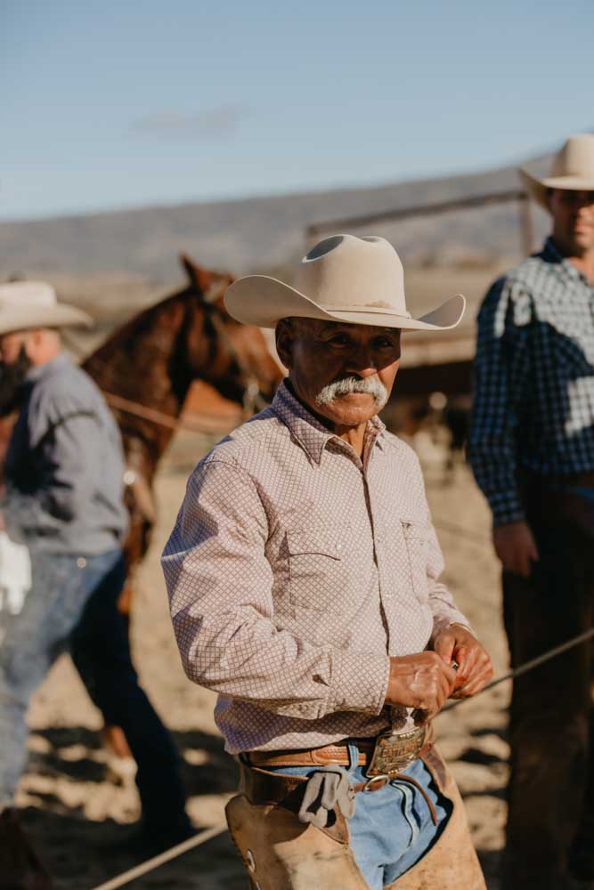 A Hearst Ranch cowboy wears a white cowboy hat, red striped shirt, and looks into the camera.